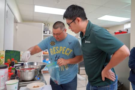 UOG meat scientist Leo Liu watches as a participant seasons pork at BBQ Bootcamp workshop.