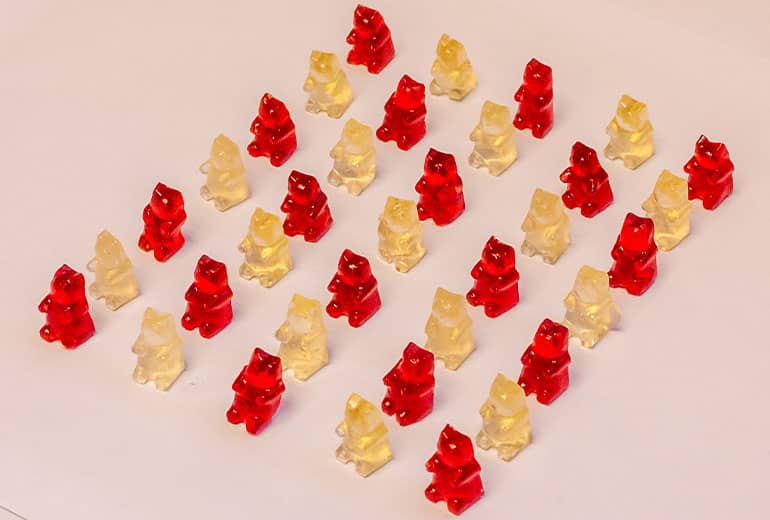 An array of red and yellow dragonfruit gummy bears sit on a plain surface