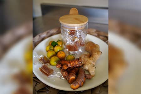 Tumeric candies sit in a jar on a plate next to ginger and calamansi