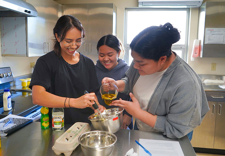 Photo of 3 students in a classroom kitchen with a mixing bowl.