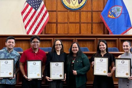 Group photo in legislative chamber with six people holding resolution certificates