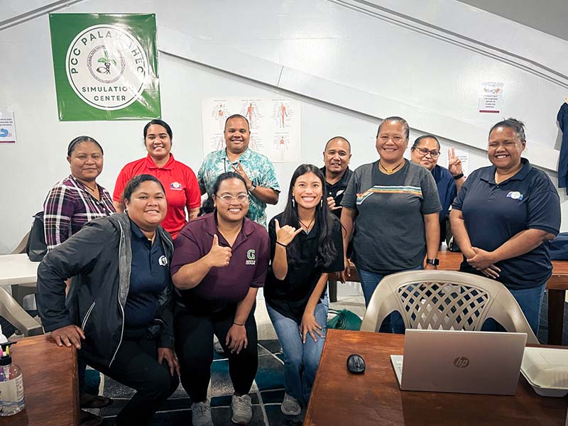 UOG graduate students Maria Minas and Cabrini Aguon with their data science workshop participants at the Palau Area Health Education Center at Palau Community College. A group photo in a classroom with a Palau AHEC banner
