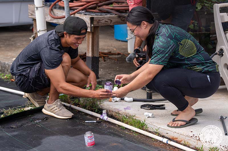 UOG CIS Island Conservation Lab staff Brian Anderson and Aubrie Uson help one another apply primer to PVC pipe extensions while building a micro-irrigation system in the CIS plant nursery. Two people applying glue to a PVC pipe