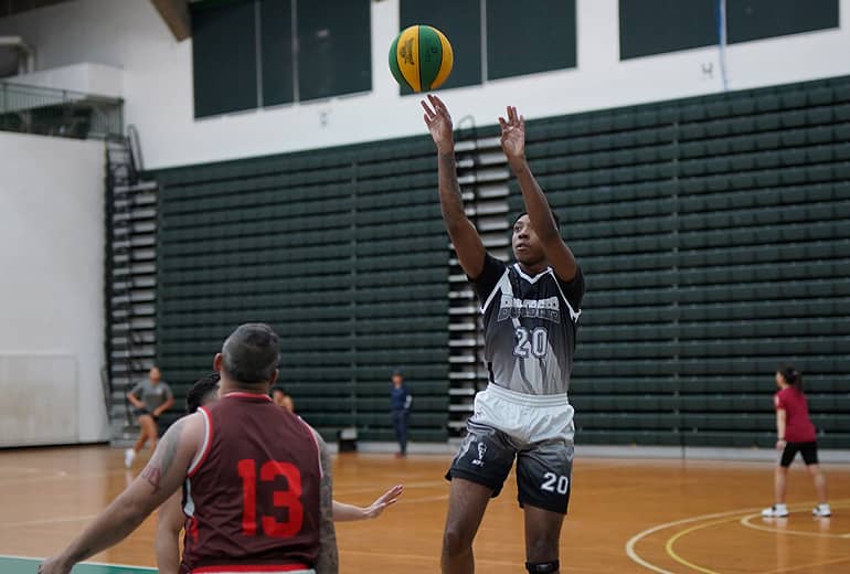 Basketball player in black and white jersey shoots basketball as opponent flanks