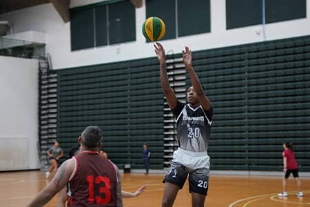 Basketball player in black jersey shoots basketball with opponent flanking