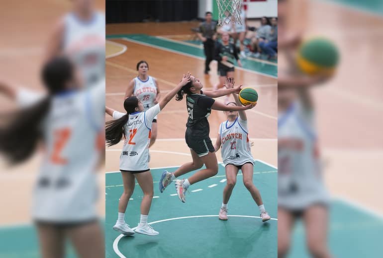 Female athletes in white jerseys attempt to block shot made by athlete in dark green jersey 