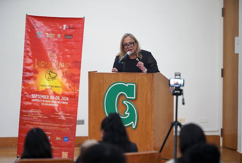 Dr. Sharleen Santos-Bamba speaks at podium next to large Lion King poster