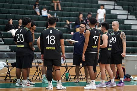 Coach talks with several team members on floor of UOG fieldhouse