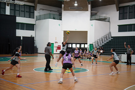 Volleyball players prepare to go for ball during game at UOG fieldhouse court