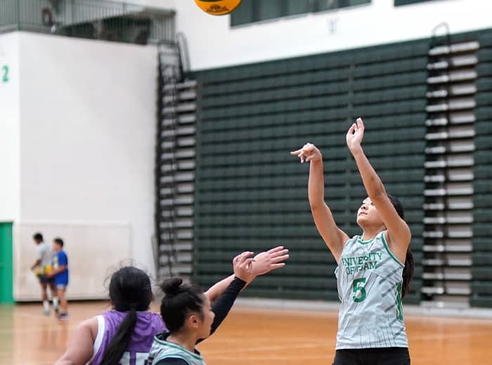 #5 in gray jersey shoots basketball while team member and opposing team member come close