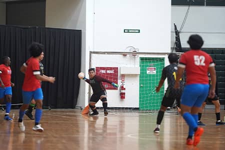 Player, net behind him, prepares to launch ball with hand as other players surround