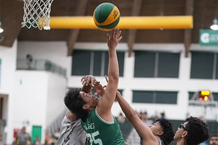 players in white jerseys try to block player in green jersey's basketball shot