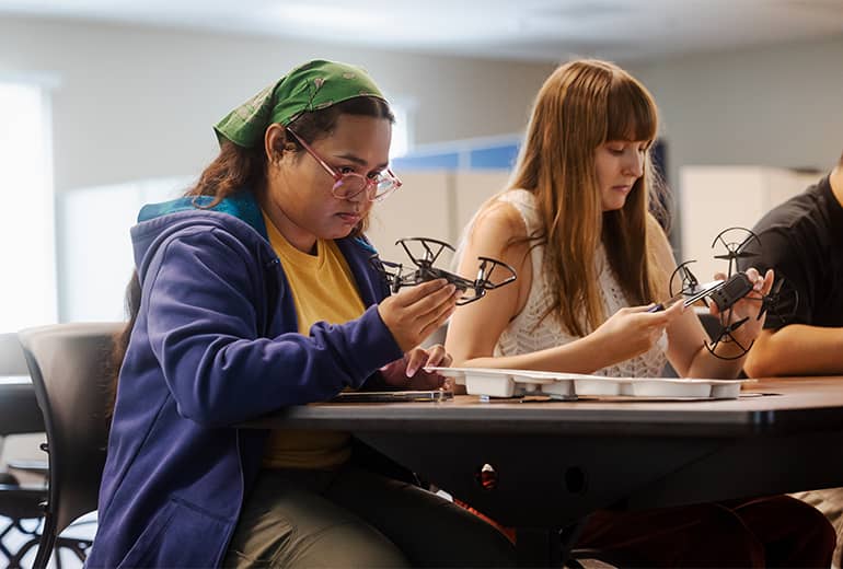 Ajalyn Omelau and Zoe Ariellius handle drone in classroom type setting during knowledge course