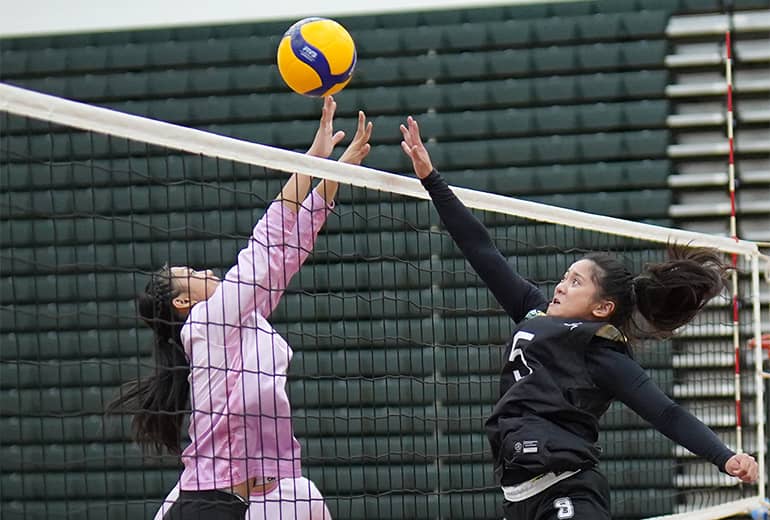 Player #5 in black spikes to blocking opponent in pink