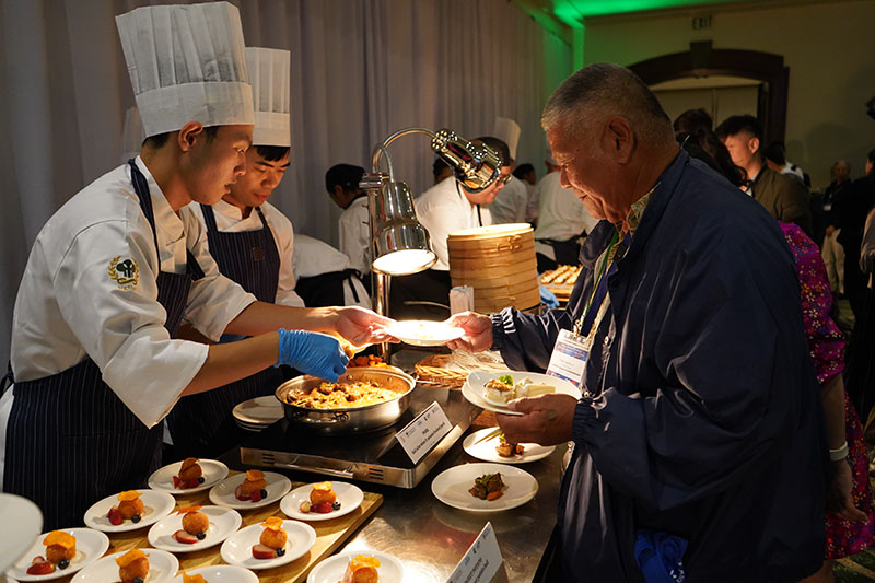 Students from National Kaohsiung University of Hospitality & Tourism in Taiwan dish up a red wine miso and sesame braised pork during a culinary dinner event at the 2025 Guam Farmer Focus Conference on Oct. 30, 2025, at the Hyatt Regency Guam. A student chef putting food on a man's plate